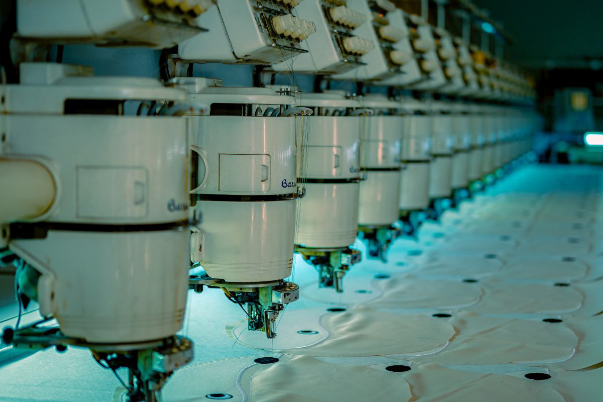 Close-up of an industrial embroidery machine stitching a red heart design with black detailing onto white fabric.